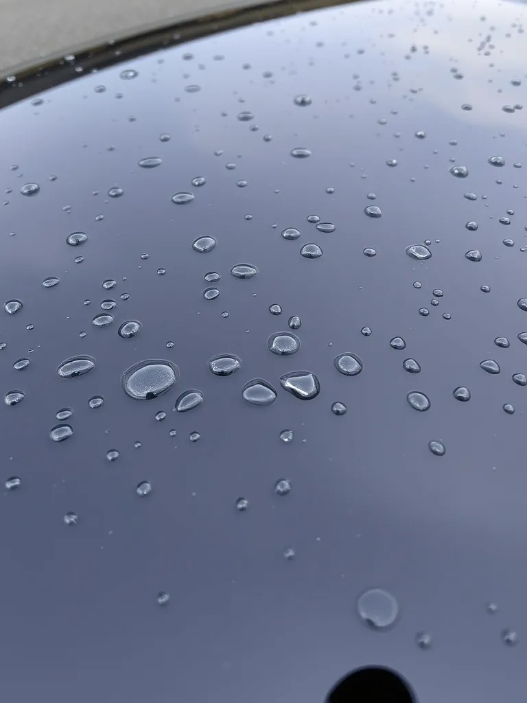 Close-up of clean water beads on a dark car hood with high g